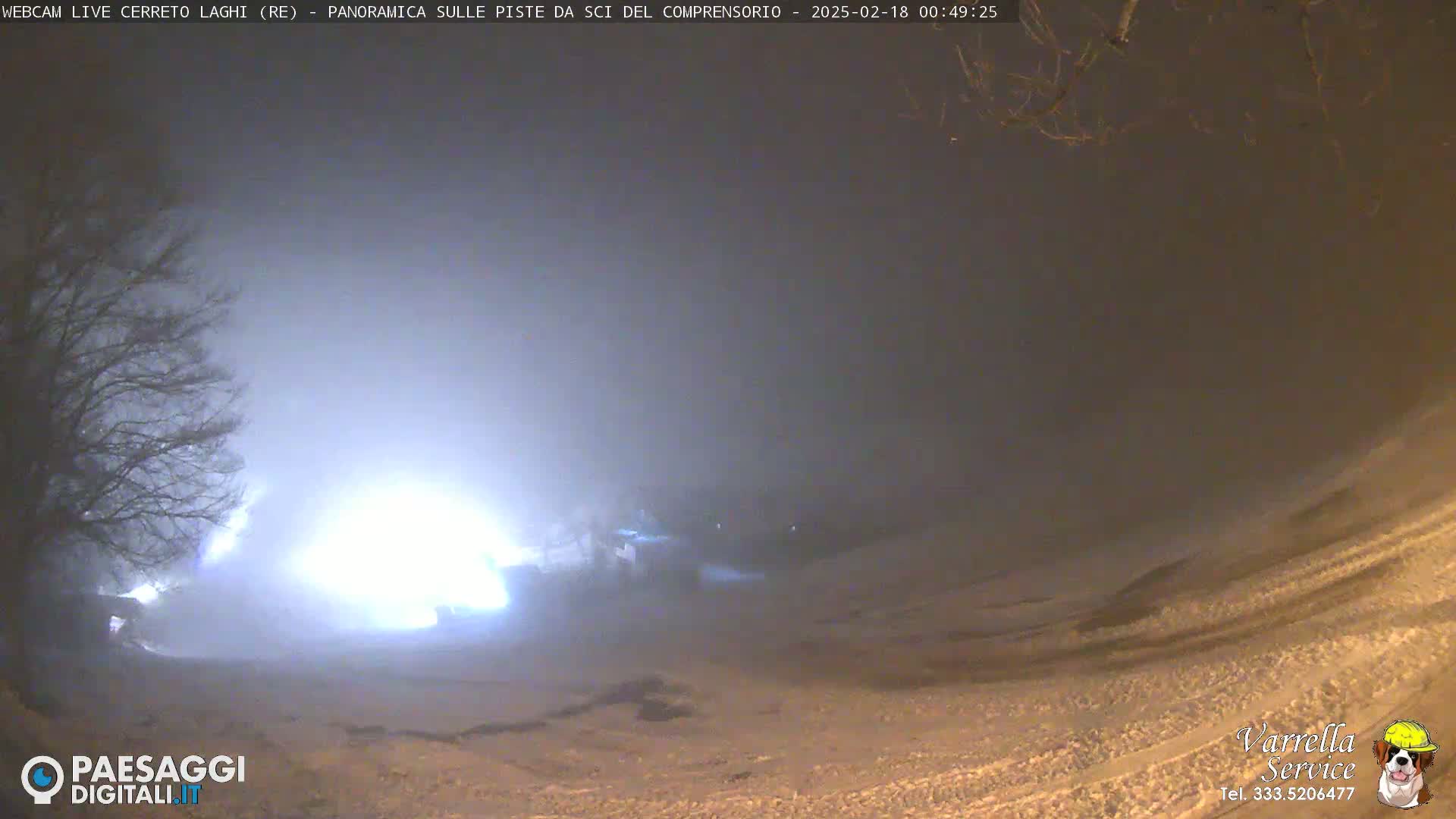 A foggy night scene shows a snow-covered slope with dimly lit structures in the distance.