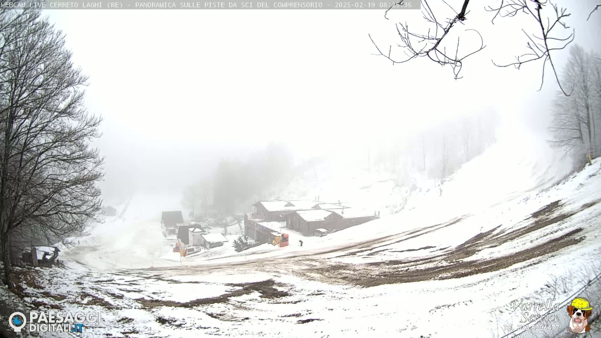 A snow-covered ski slope with several buildings at the bottom, viewed on a foggy day.