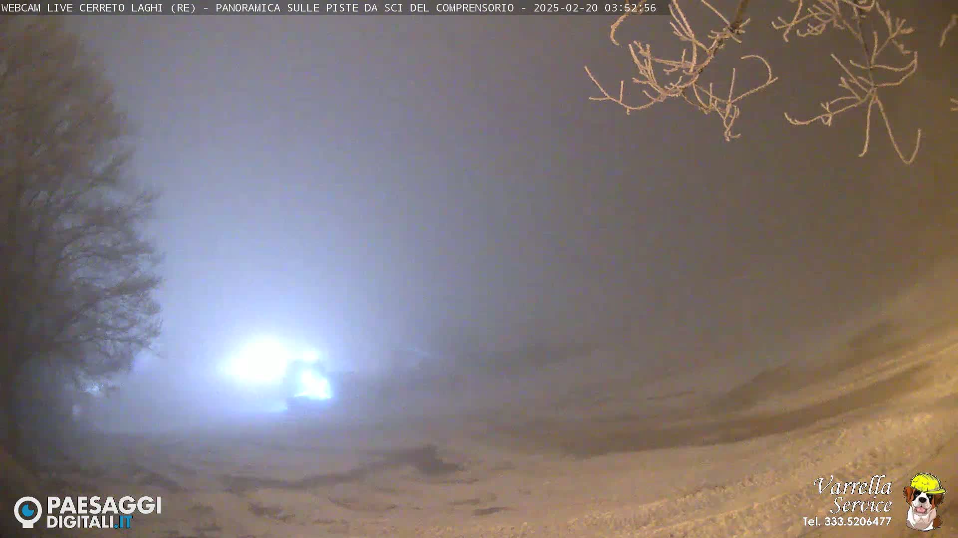 A snowy landscape is shrouded in thick fog under a dark sky, illuminated by a bright light source in the distance.