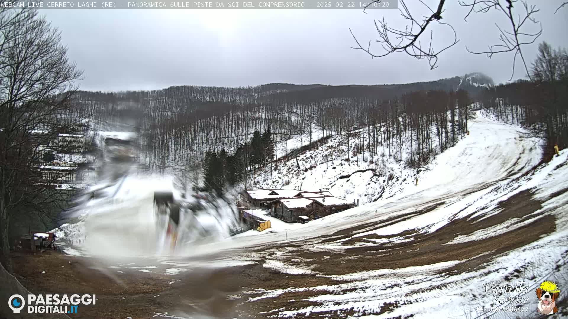 A snow-covered ski slope with a few buildings in the background on an overcast day.