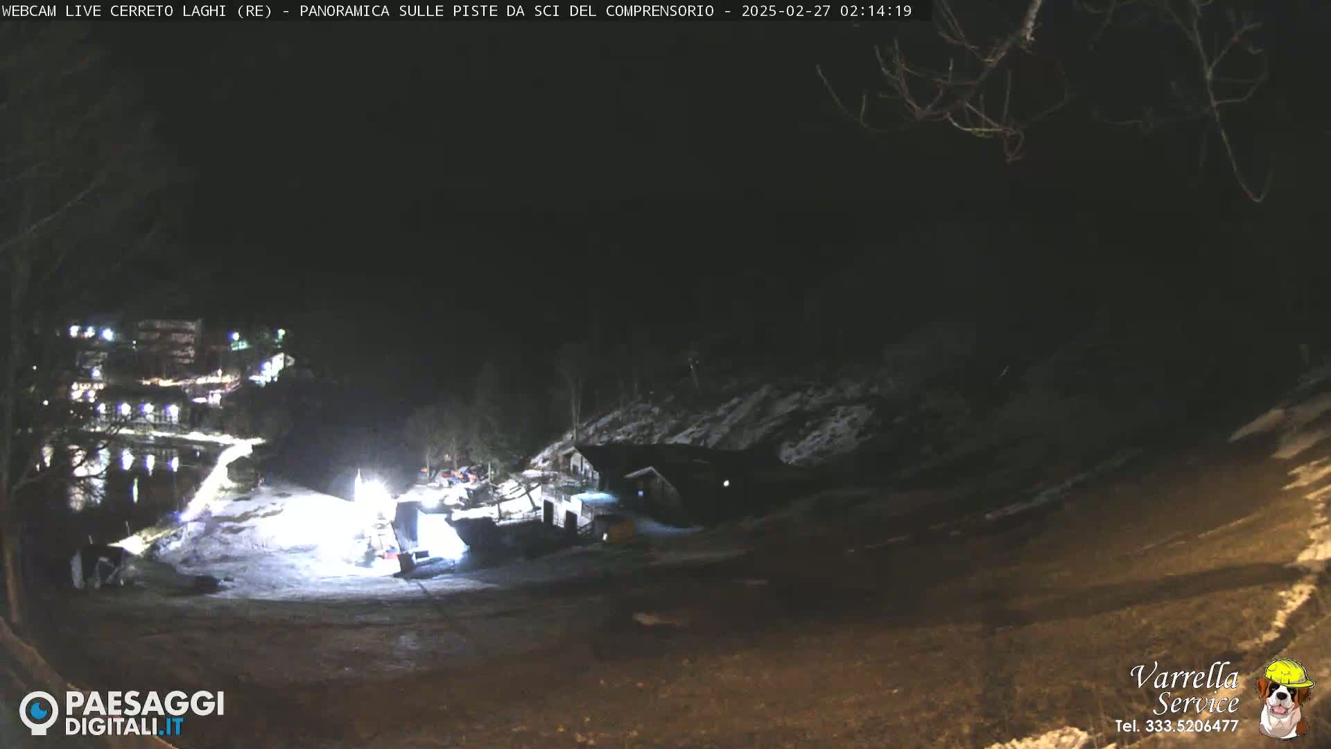 A nighttime view of a snow-covered slope with a building and some vehicles illuminated by artificial lights.