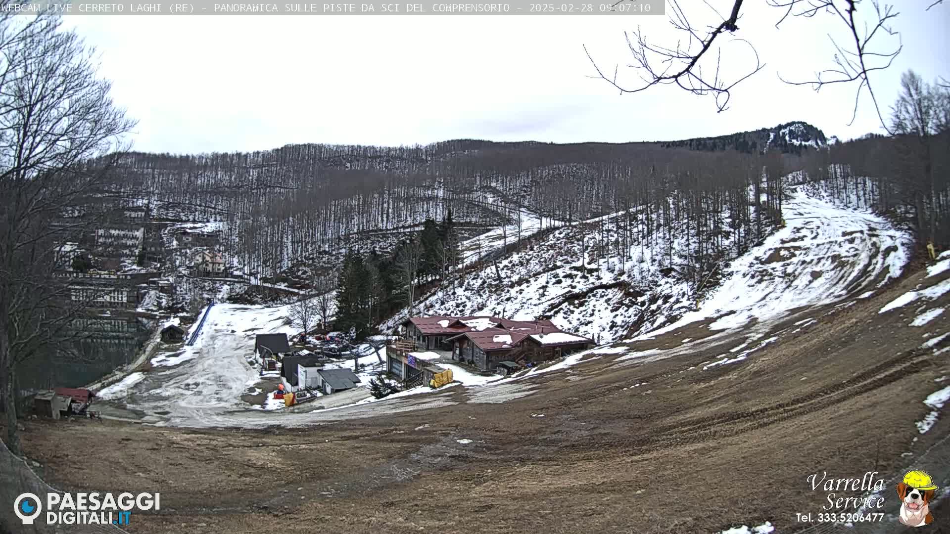 A mostly cloudy day reveals a snow-dusted ski resort nestled in a mountain valley, with a few buildings visible near the base of the slopes.