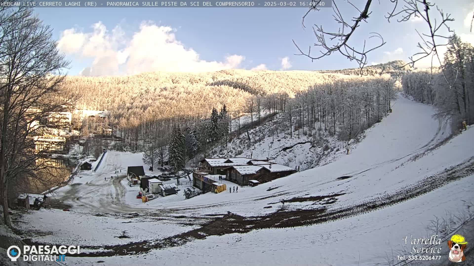 A snow-covered ski slope and surrounding wooded hills are visible under a mostly clear, sunny sky.