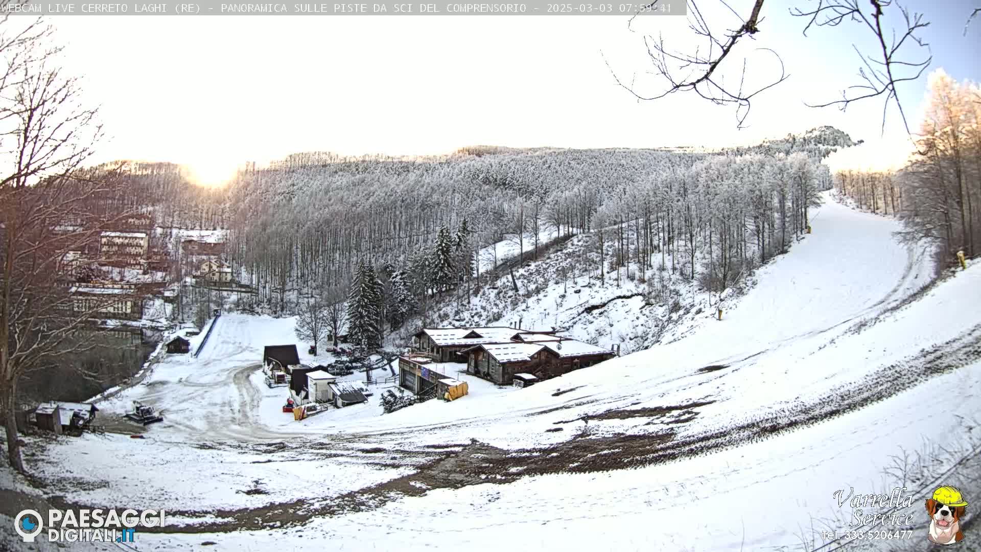 A snow-covered ski slope with several buildings at its base, situated amongst a snow-dusted forest under a clear, bright sky.