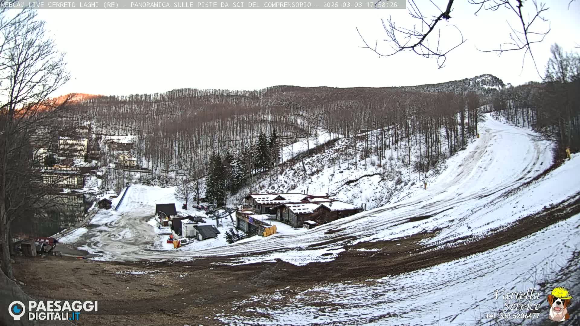 A snowy hillside with a cluster of buildings and ski slopes visible under a mostly clear sky.