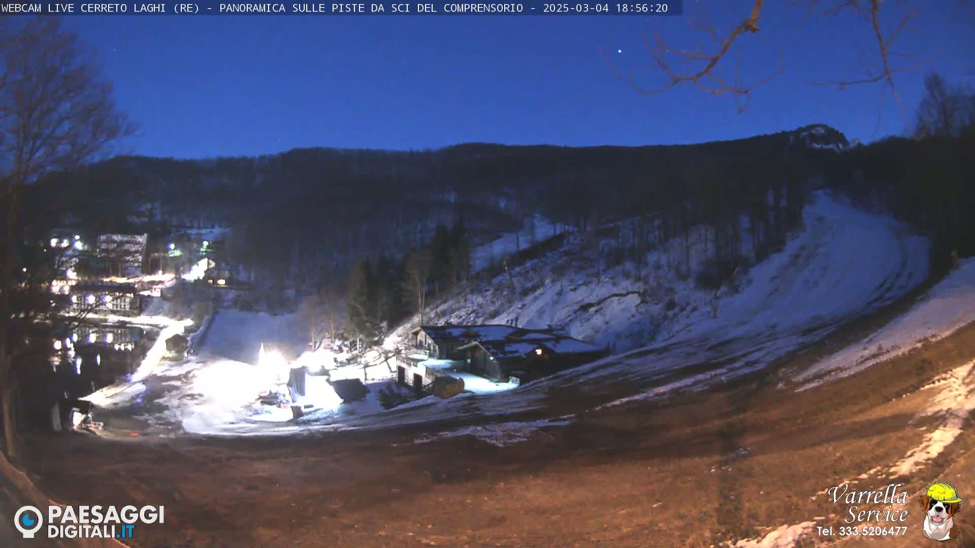 A nighttime view of a snow-covered ski slope with a building illuminated, under a twilight sky.