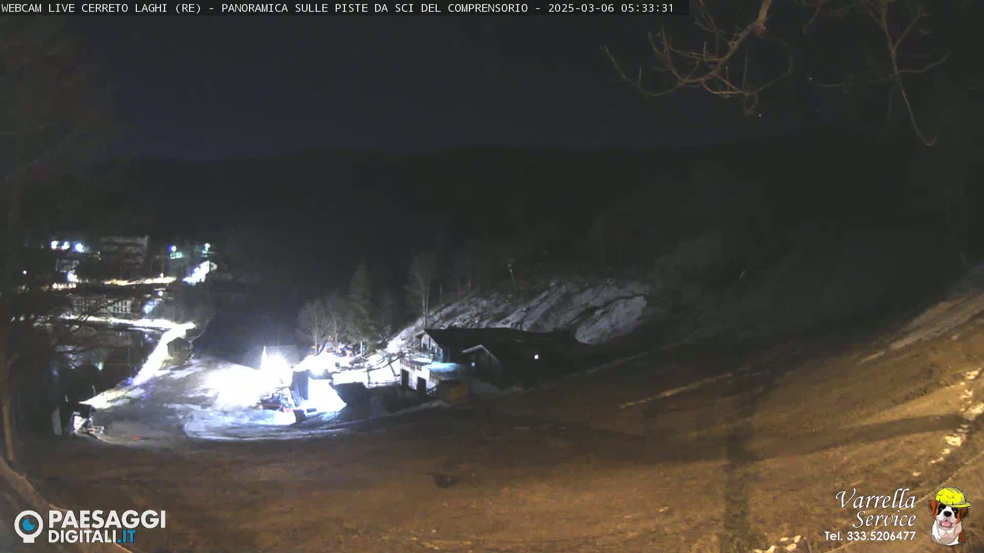 A nighttime, snow-dusted hillside scene shows a ski resort with illuminated buildings and pathways.