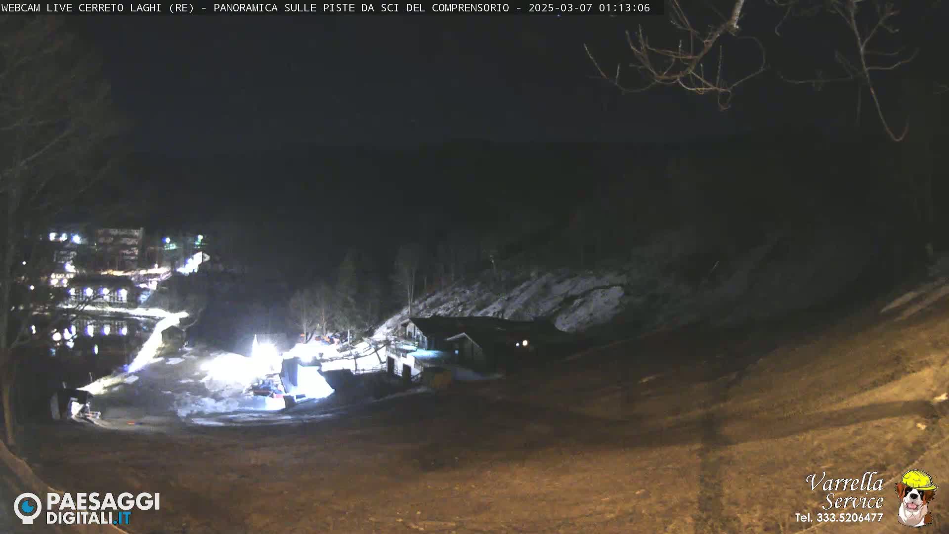 A nighttime view of a snow-covered slope with a building and several lights illuminating the area.