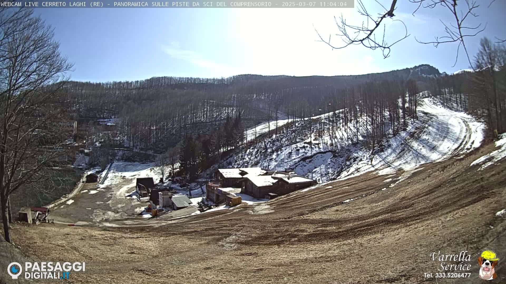 A sunny view of a snow-dusted ski slope and resort building nestled in a wooded hillside.