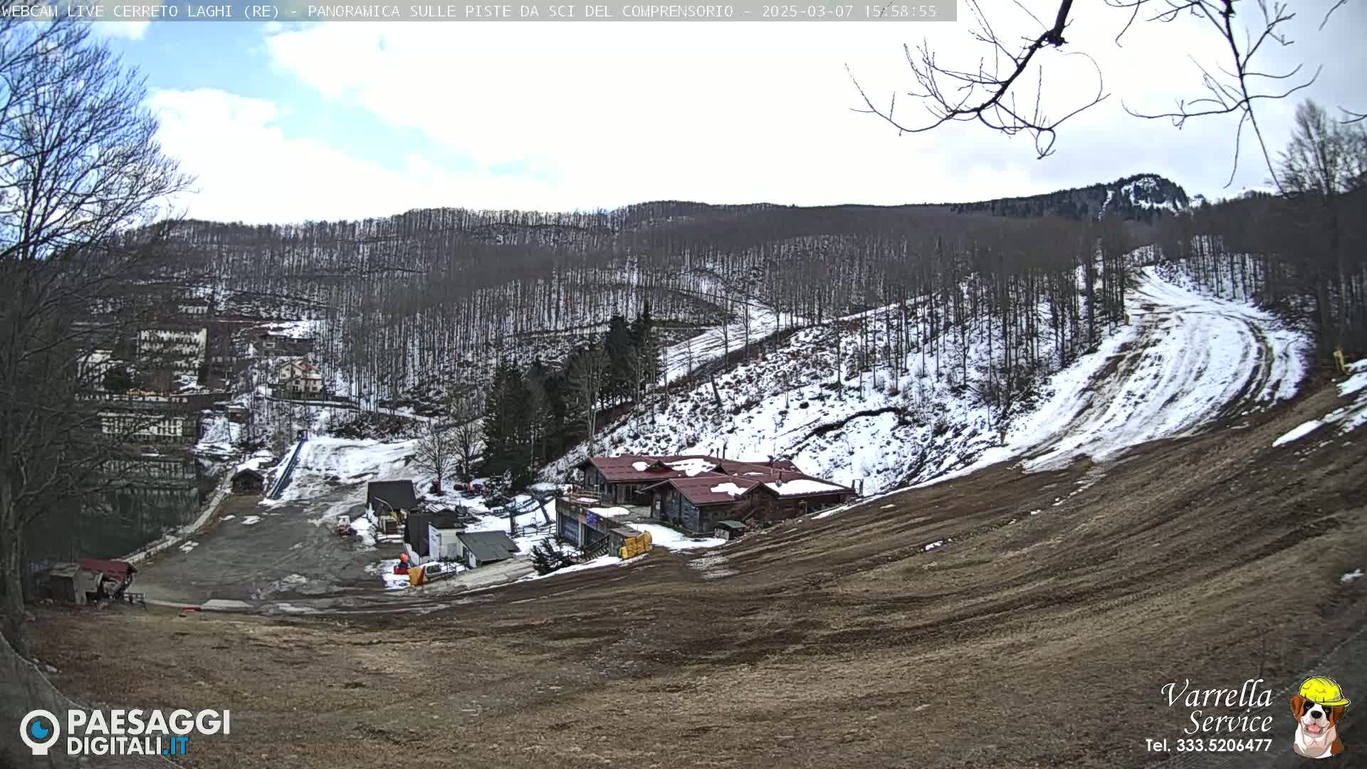 A mostly clear day shows a snow-covered ski slope and surrounding woods with a cluster of buildings at the base of the hill.
