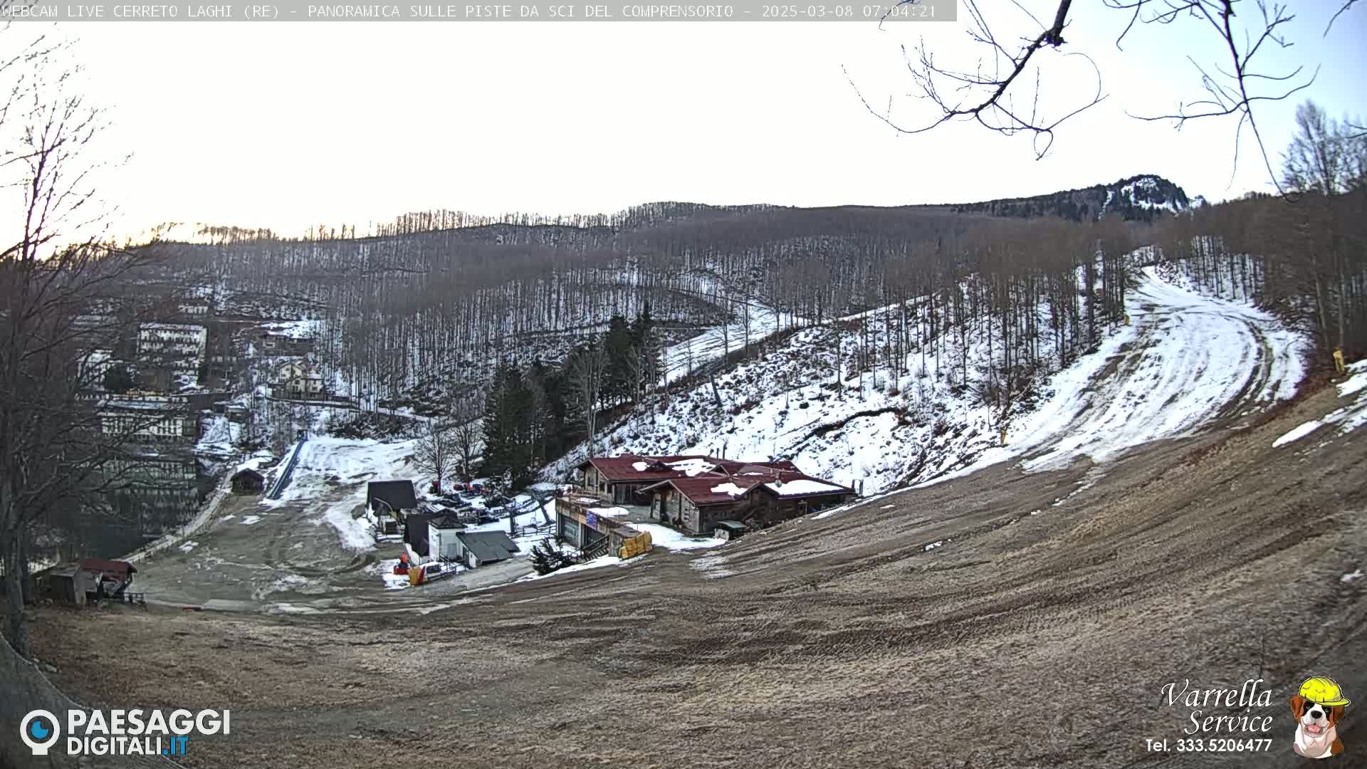 A partially snow-covered ski slope with a building at the base, under a mostly clear sky.