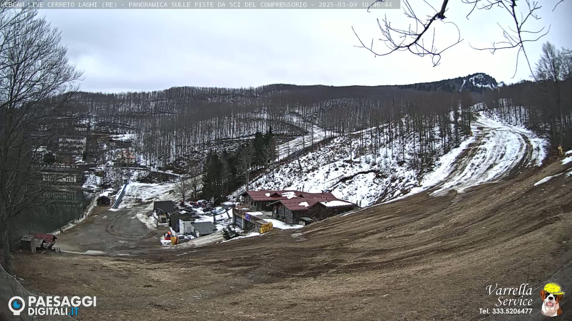 A mountainside ski resort with patchy snow cover under an overcast sky is visible from a high vantage point.