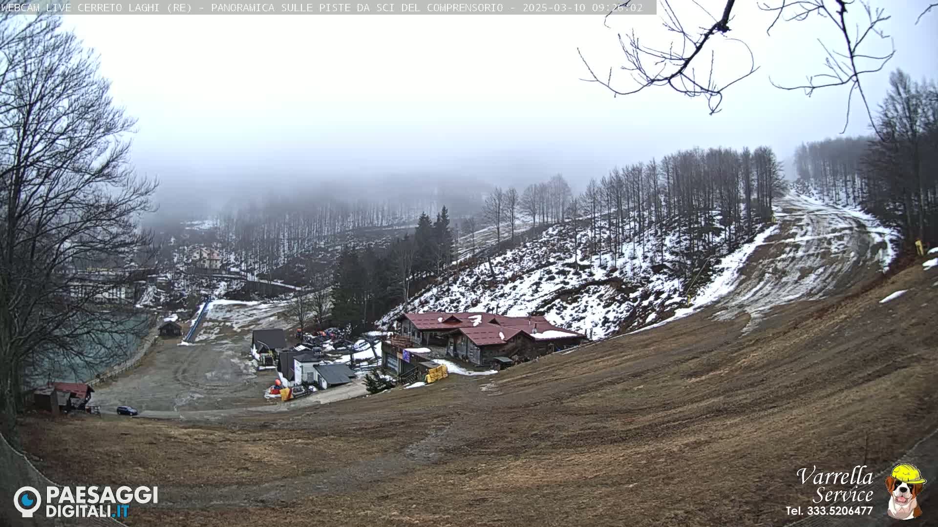 A foggy, snowy hillside ski resort with a few buildings and sparse snow cover on the slopes.