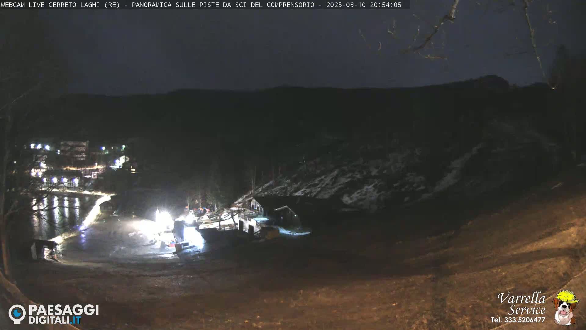 A nighttime view of a snow-dusted hillside near a body of water, illuminated by artificial lights.
