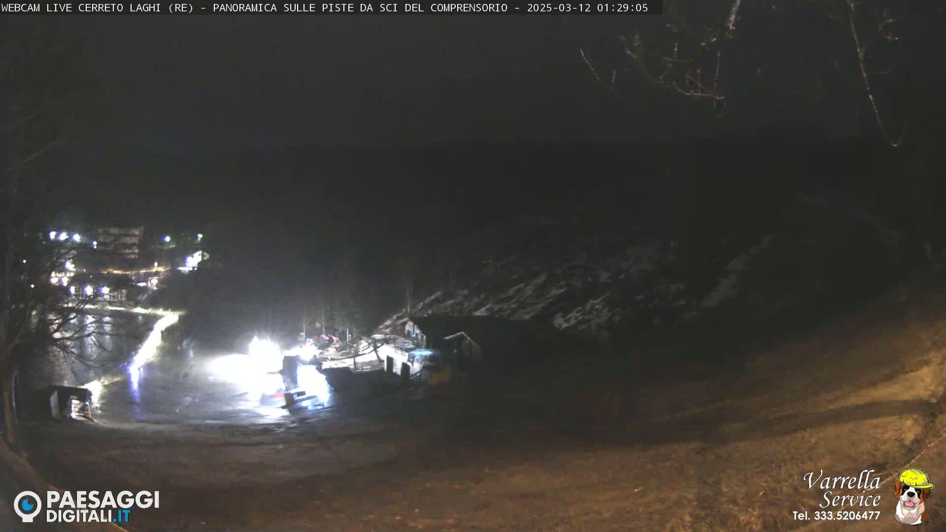 A nighttime view of a snow-covered area with a few lights visible, possibly a ski resort, under dark, clear skies.