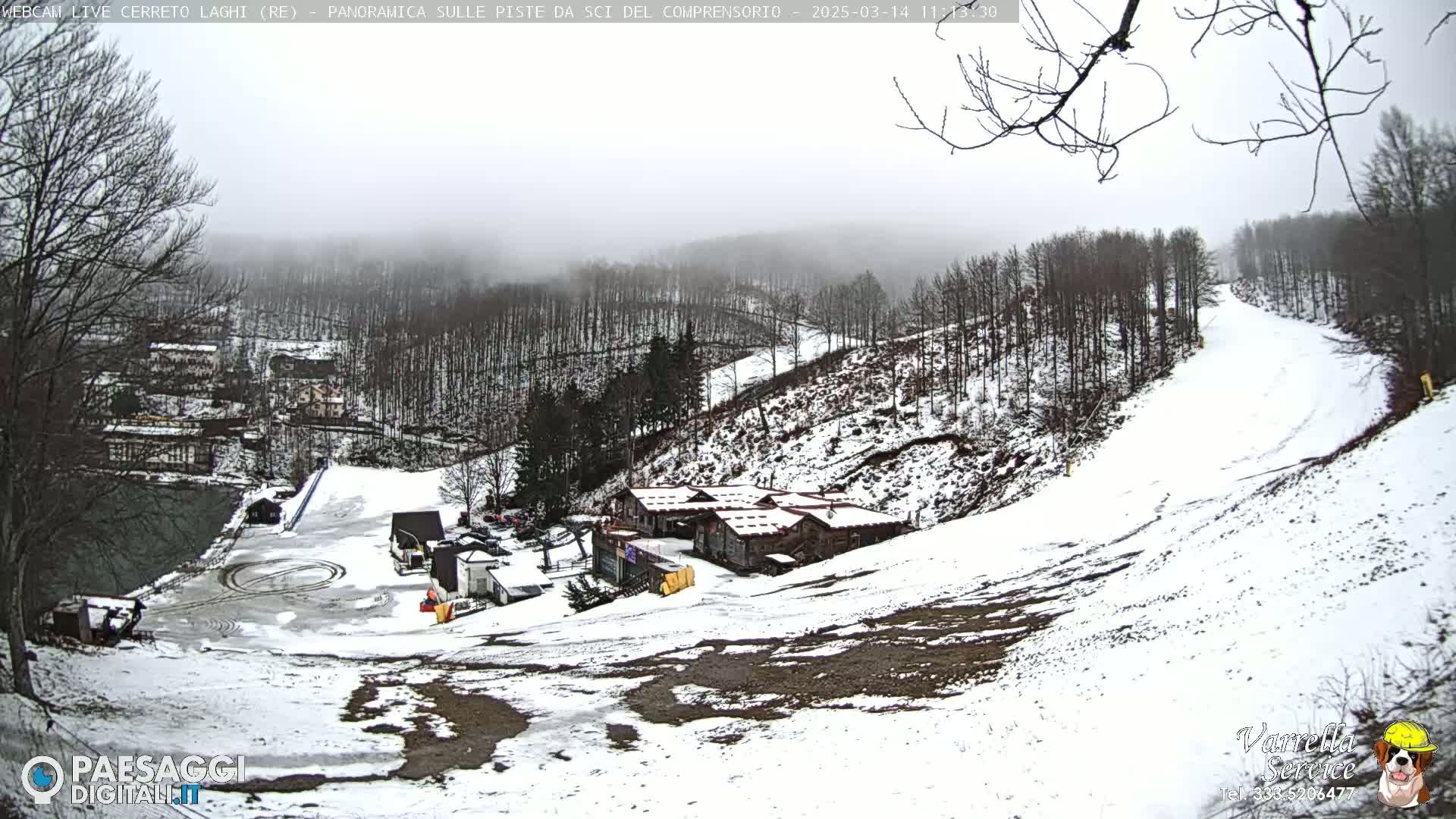 A snow-covered ski slope with a cluster of buildings and a foggy sky is visible.