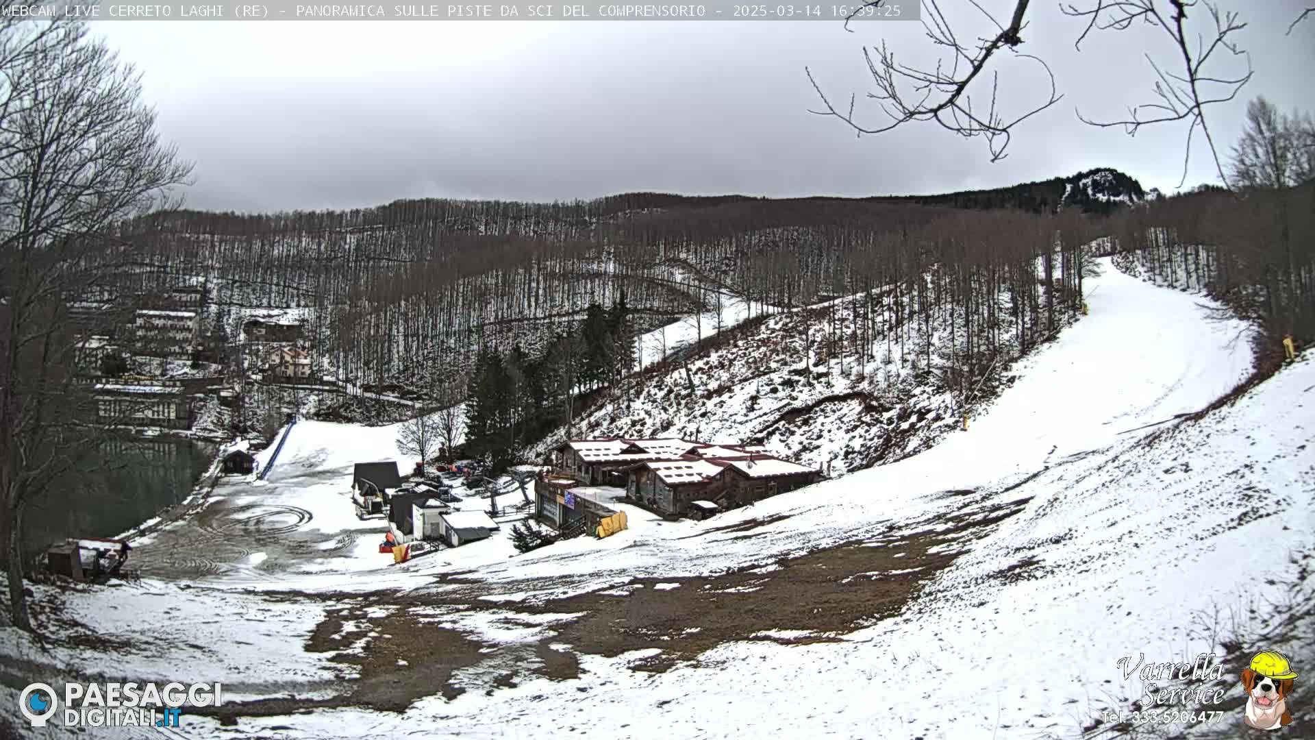 A snow-covered ski slope with several buildings at its base, under a cloudy sky.