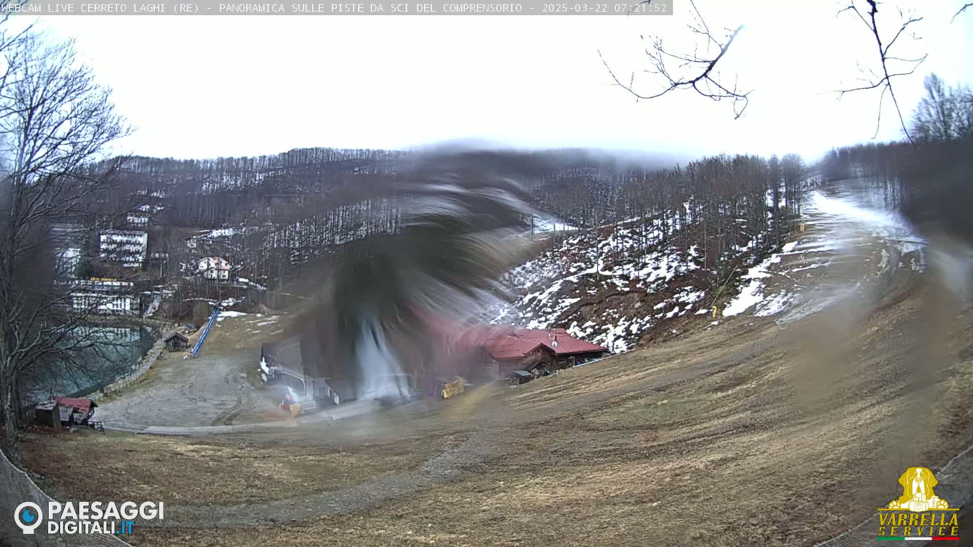 A snow-making machine sprays snow onto a ski slope in an overcast, snowy mountain setting.