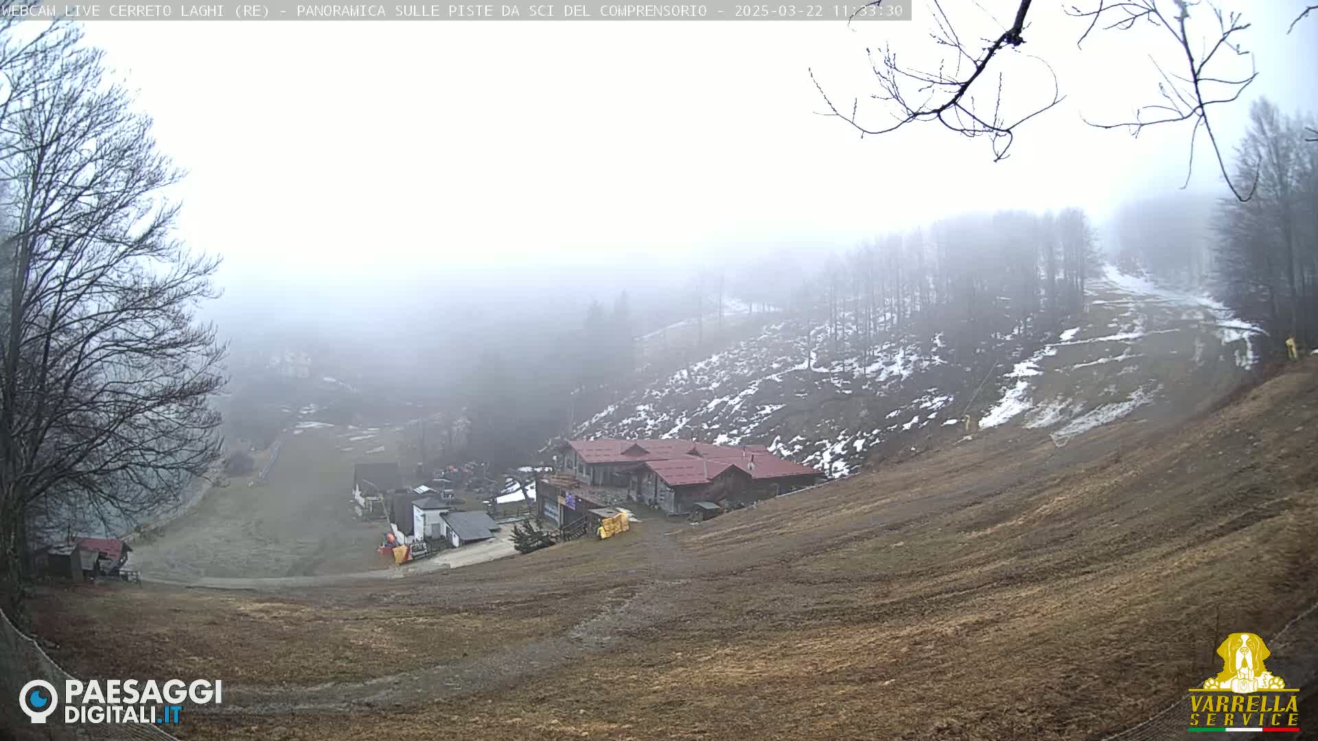 A foggy view of a ski slope with a building and sparse snow patches on a hillside.