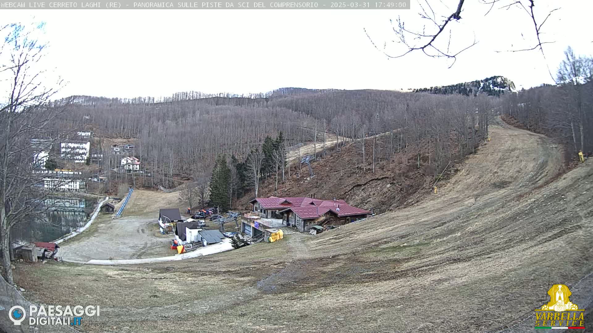 A mostly clear day view of a ski resort with a building, ski slopes, and sparse vegetation.