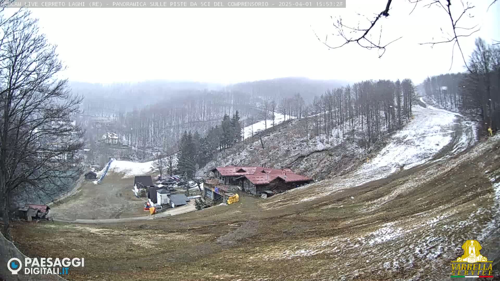 A snow-dusted ski resort with a cluster of buildings is visible, nestled among bare, snow-dappled trees under an overcast sky.
