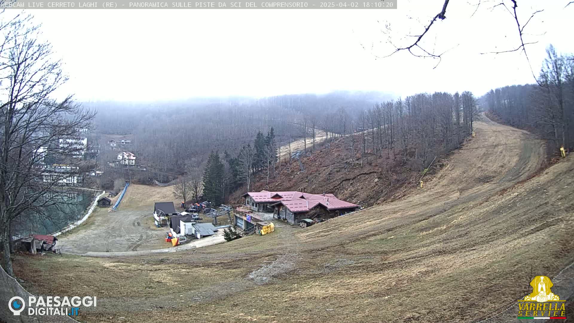 A hazy, overcast day reveals a ski slope with a brown, barren landscape, a few buildings, and a small body of water in the distance.