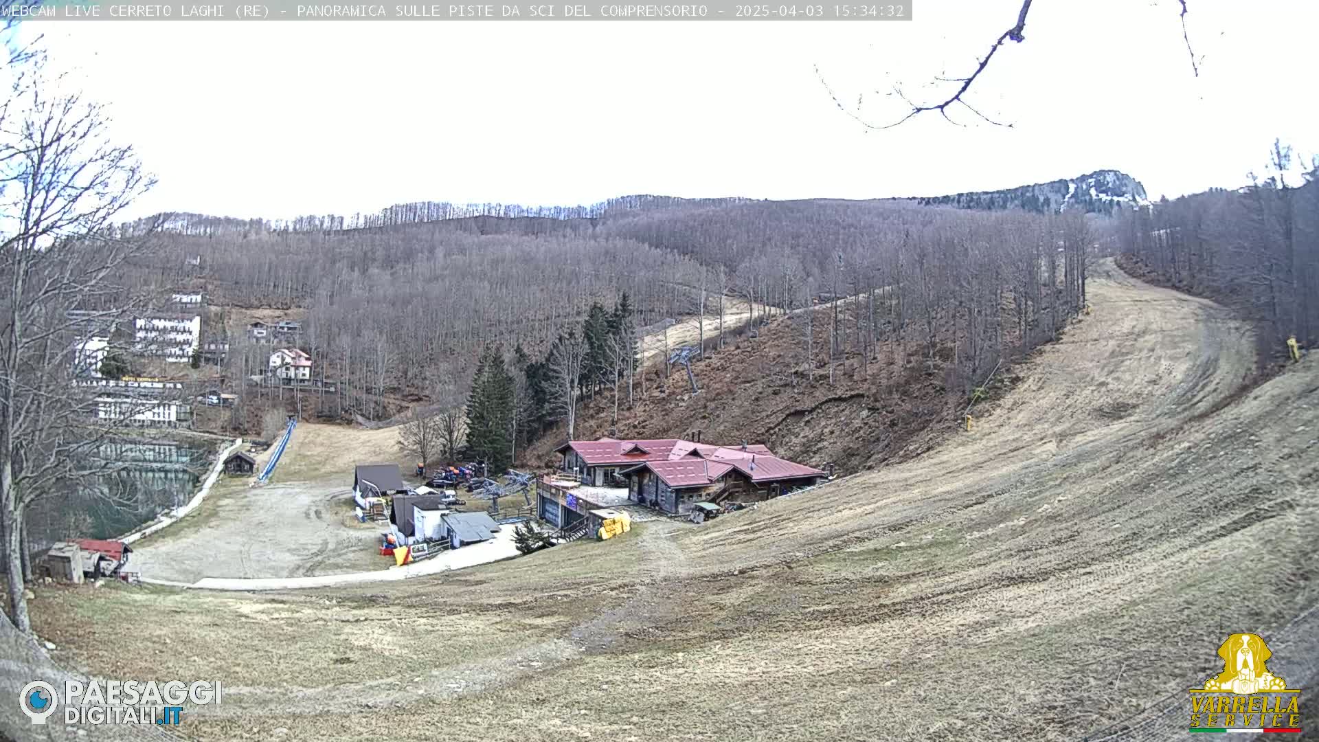 A mostly barren ski slope with a building at its base, surrounded by leafless trees under a bright, overcast sky.