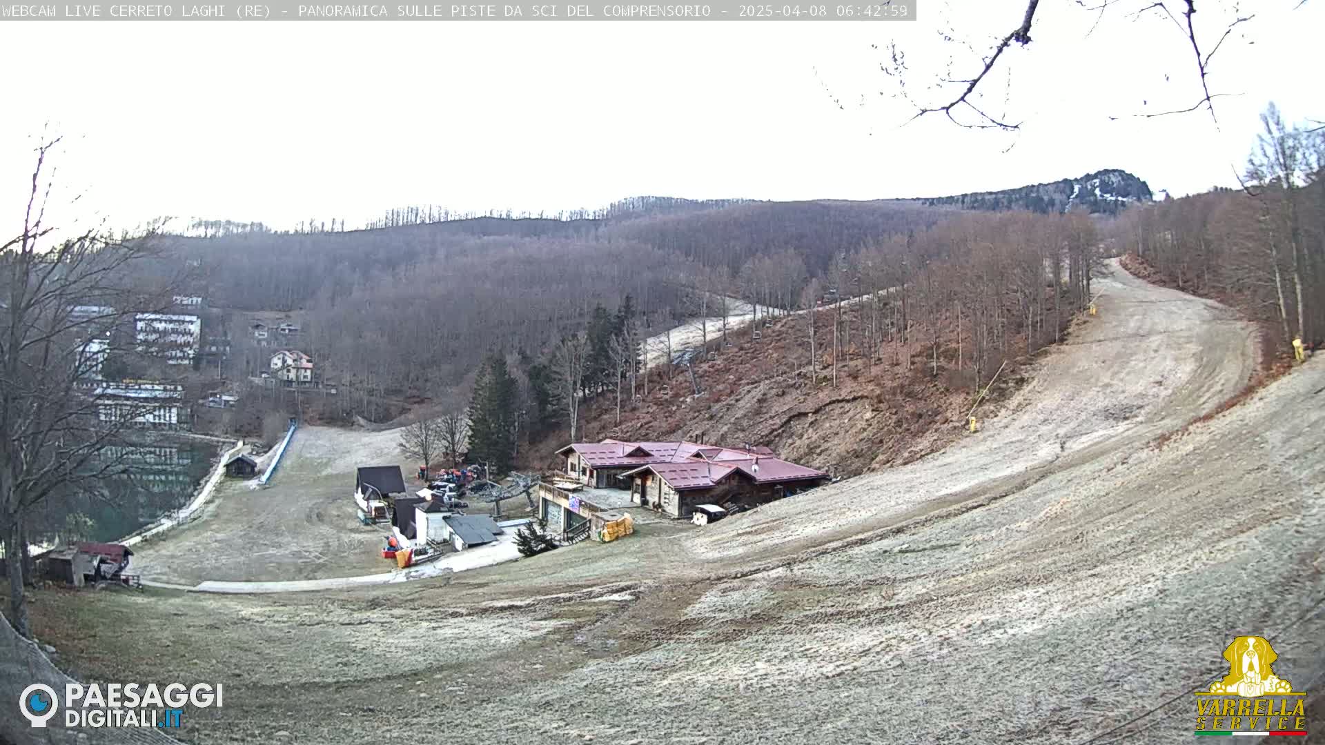 A mostly clear, cold day at a ski resort with bare, brown hills and a small building near the bottom of a ski slope.