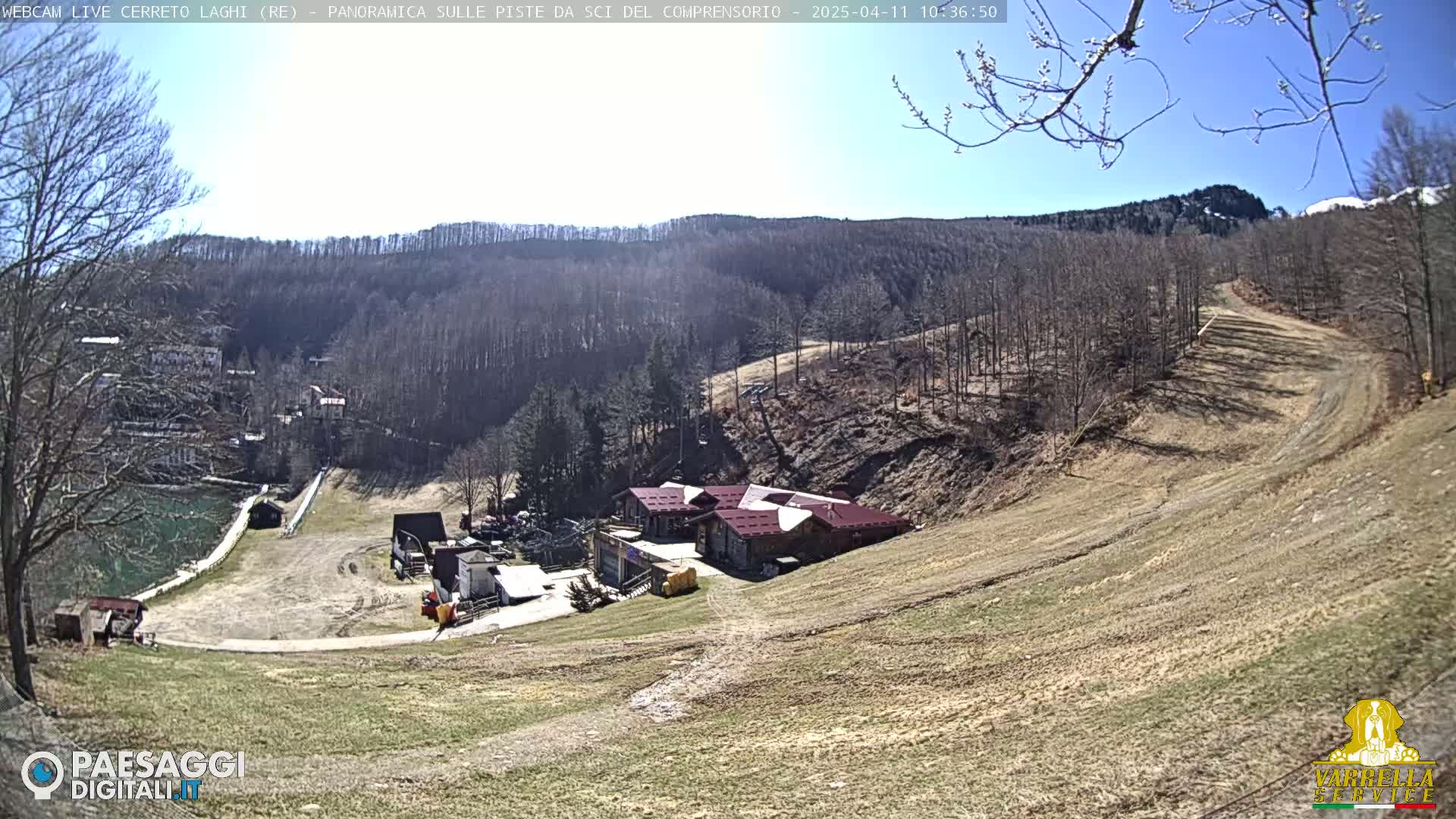 A sunny day reveals a ski resort nestled in a hillside, with barren trees and brown, grassy slopes.