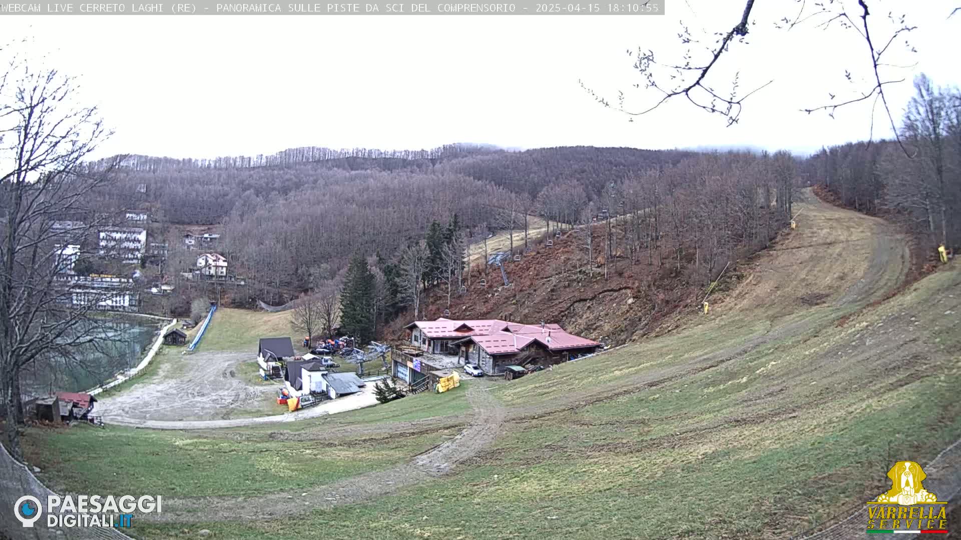 A ski resort with a red-roofed building is nestled in a hillside overlooking a valley of bare trees under an overcast sky.