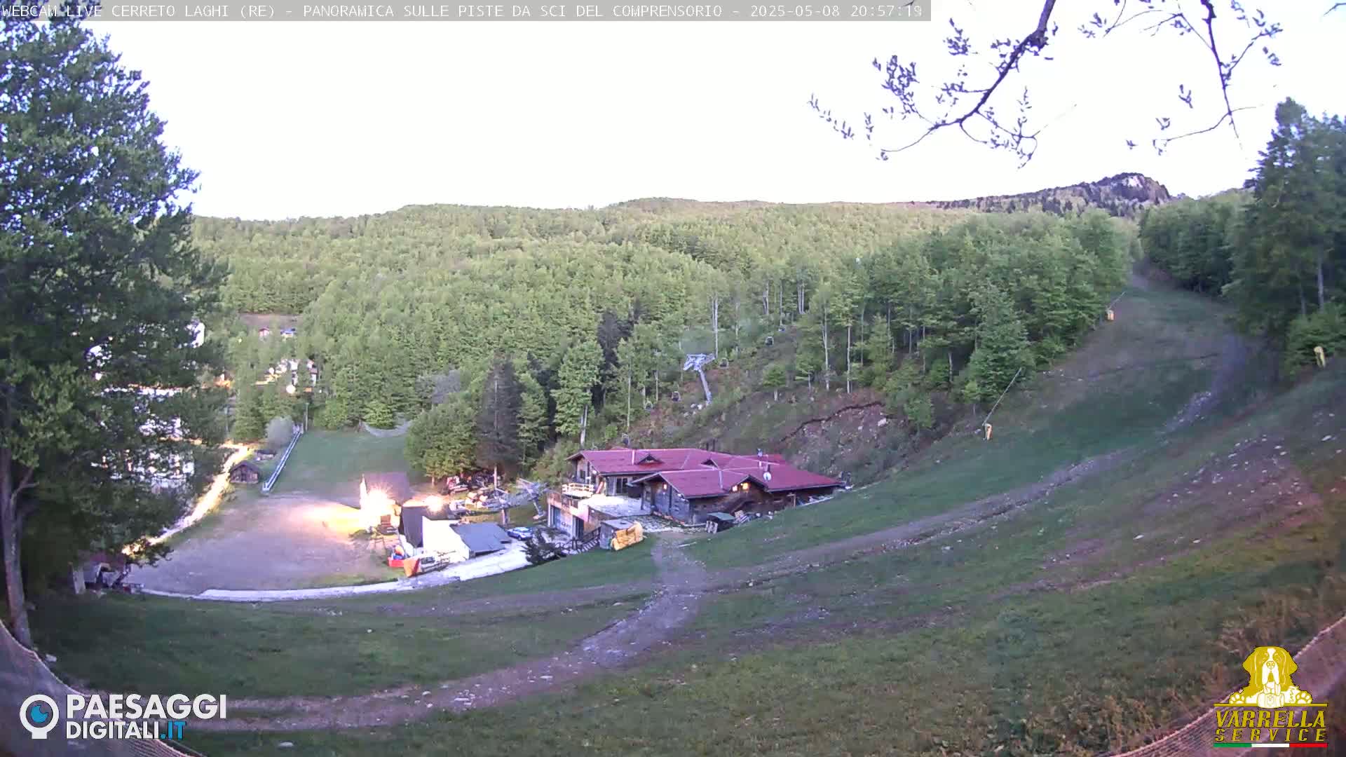 A high-angle, twilight view of a ski slope with a building at its base, surrounded by lush green trees on a hillside.