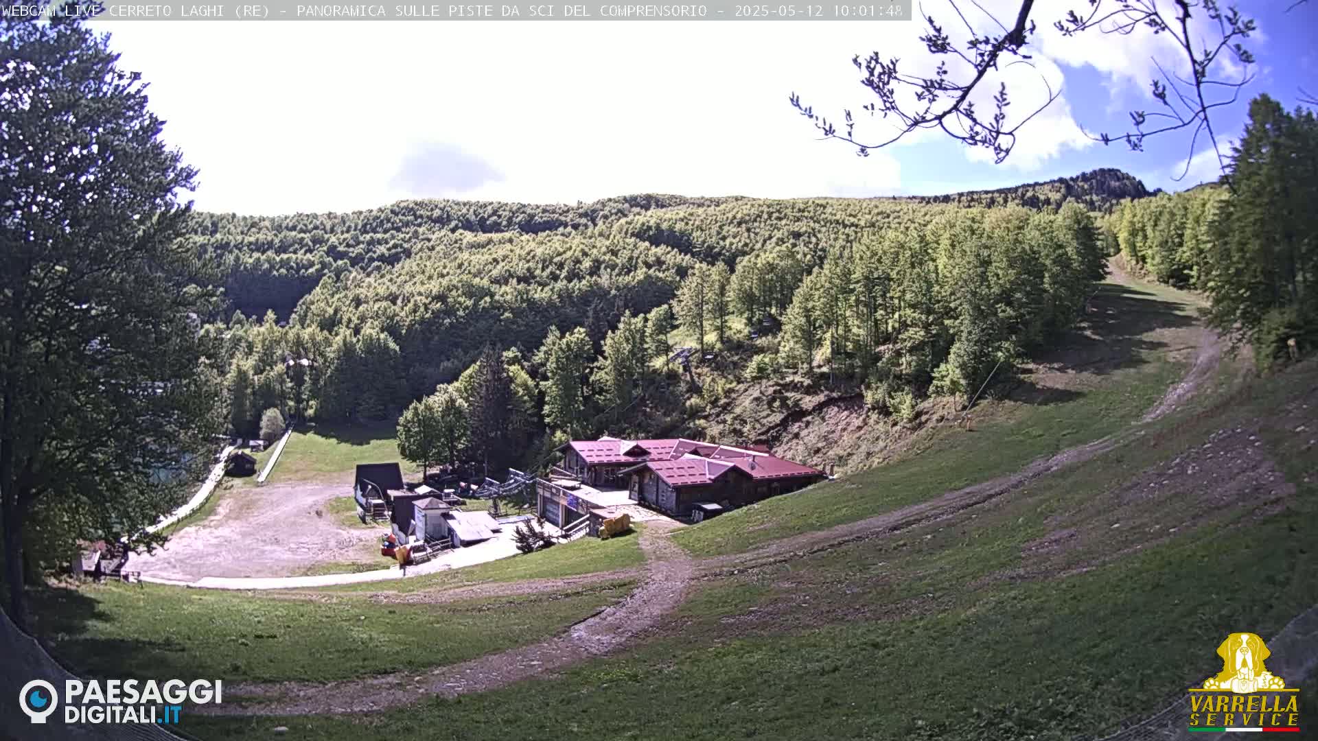 A mountainside ski resort with a building and grassy slopes is visible under a partly sunny sky.