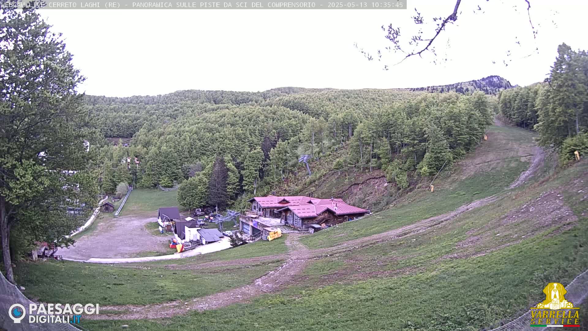 A mountainside ski resort with a building and a grassy ski slope, under an overcast sky.