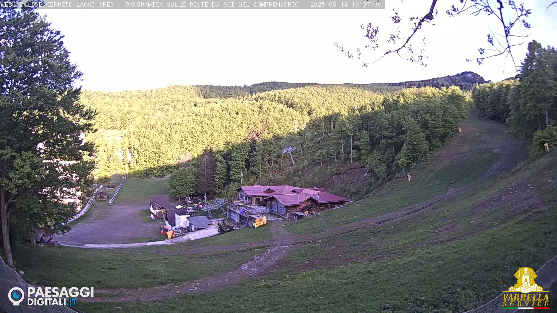 A ski slope in a forested area under a mostly clear sky, with a small building near the bottom of the hill.