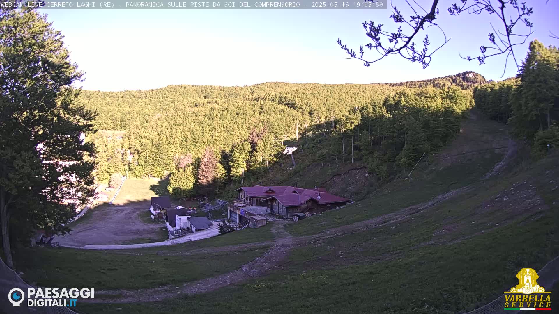 A mostly clear, late afternoon view of a ski slope with a lodge and surrounding forest.