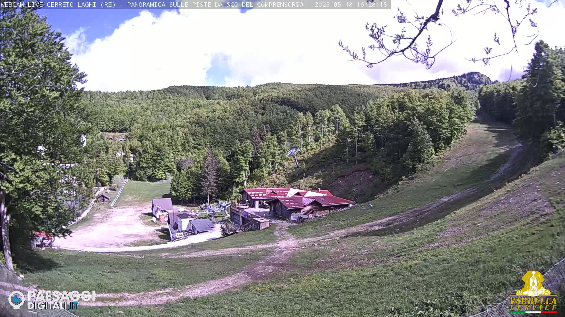 A partly cloudy day reveals a ski resort nestled in a verdant hillside, with several buildings and a ski slope visible.