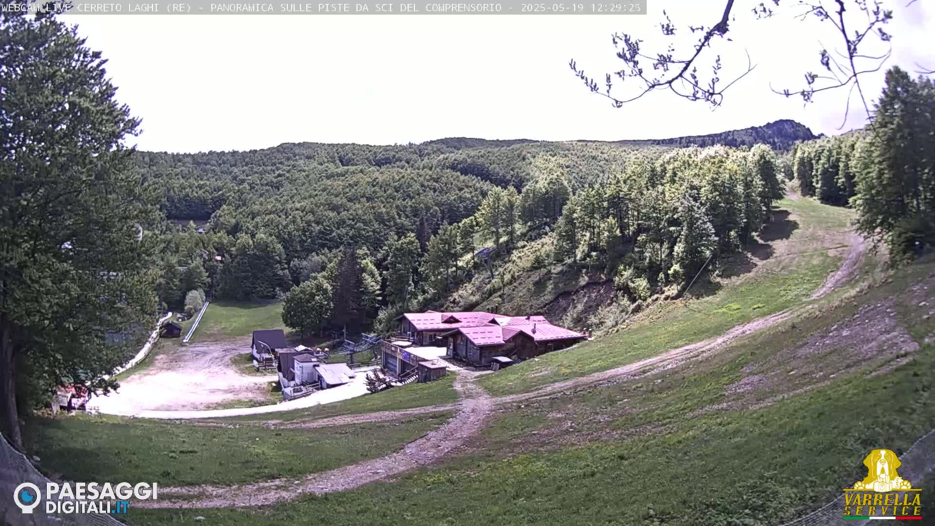 A grassy hillside with a cluster of buildings and a ski slope visible under a mostly clear sky.