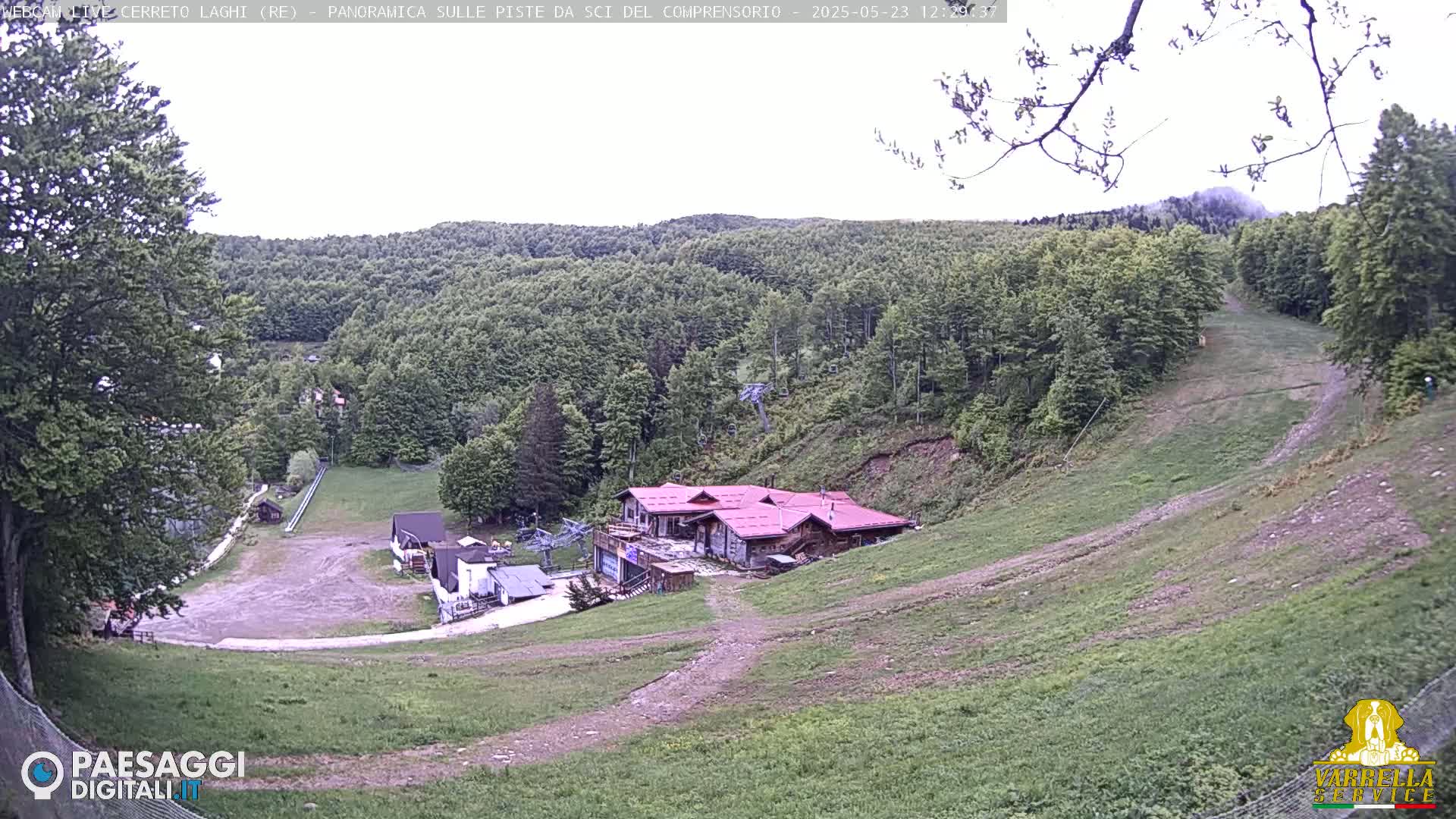 A mostly cloudy day reveals a ski resort in the hills, featuring several buildings and grassy ski slopes.