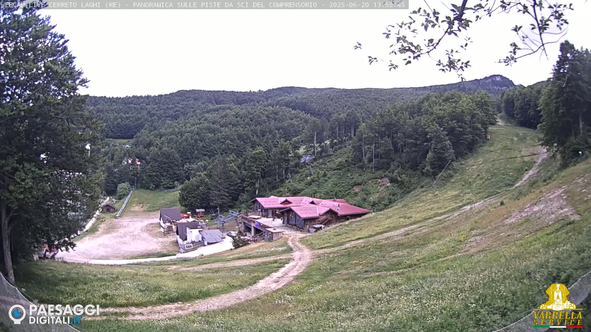 A ski resort in a mountain range on an overcast day, with a building at the bottom of a grassy ski slope.