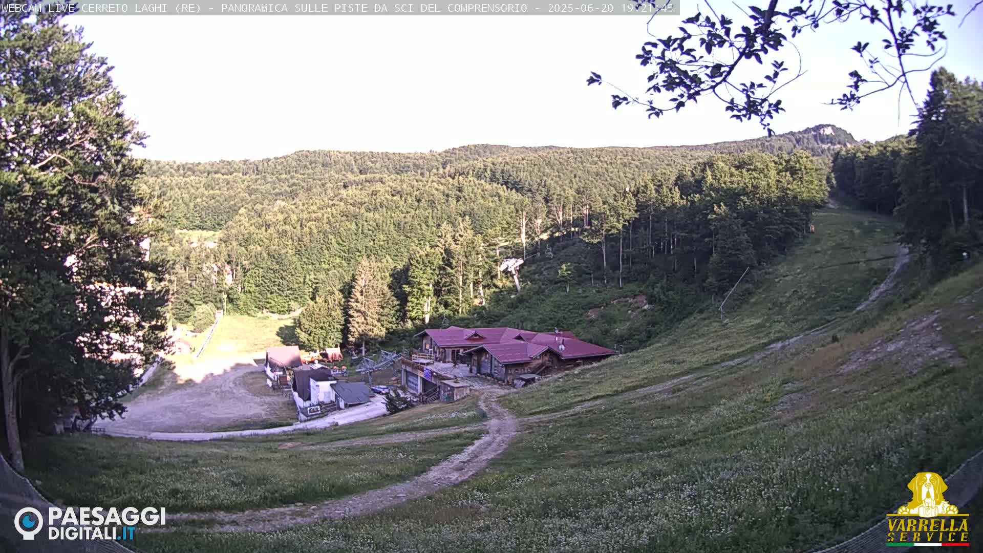 A grassy hillside with a building and ski lift visible, under a mostly clear sky.