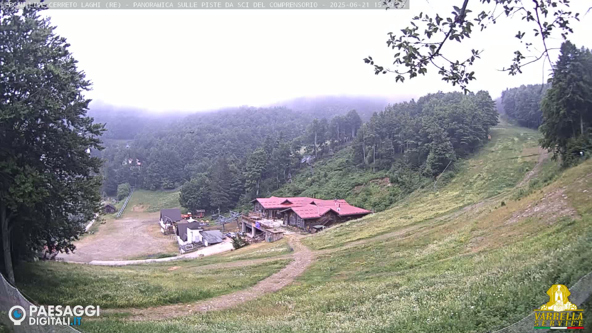 A foggy mountain slope with a red-roofed building and grassy areas, viewed from above.