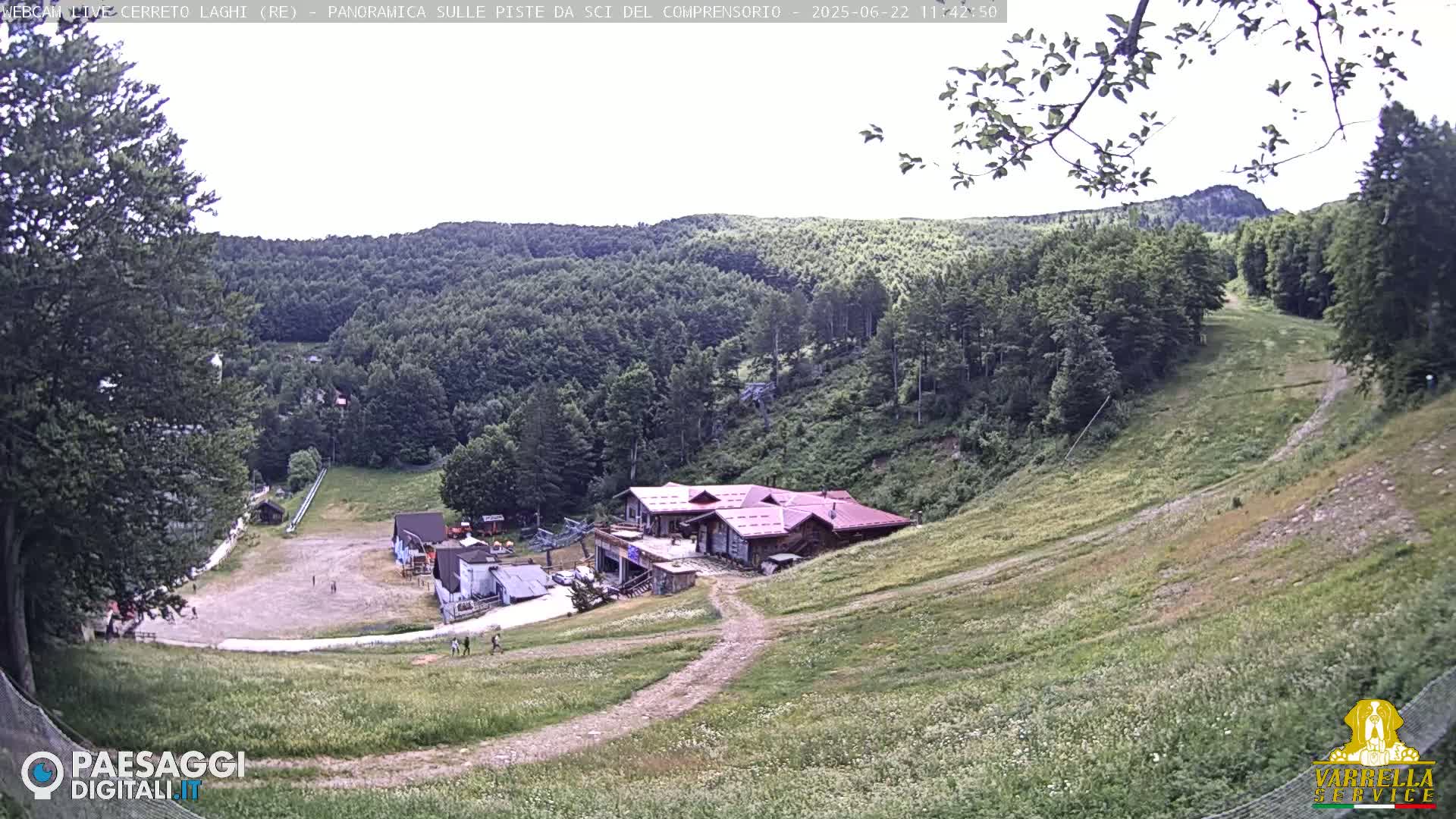 A mountainside ski resort with a main building and grassy slopes is visible on a partly cloudy day.