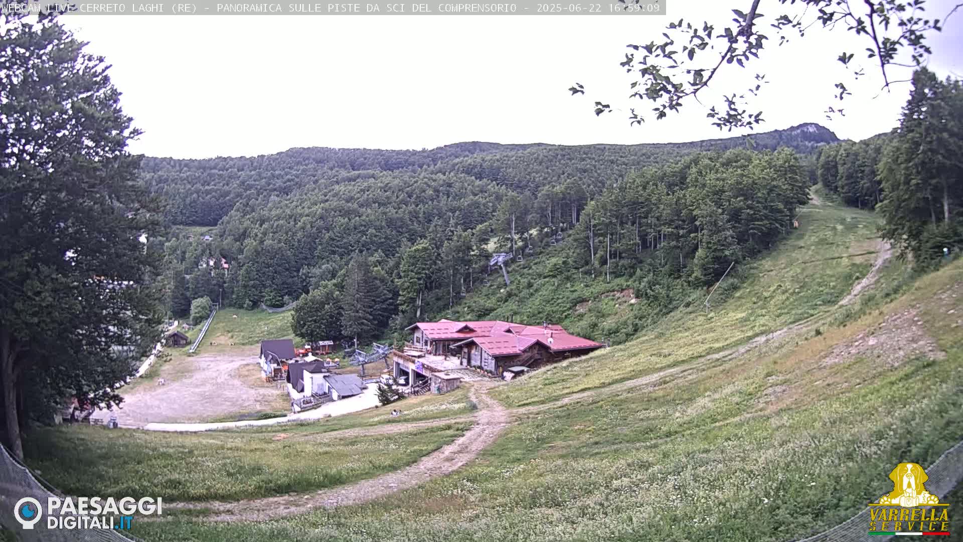 A ski resort in a mountainous area, mostly covered in green vegetation, with a building near the bottom of a grassy slope under an overcast sky.