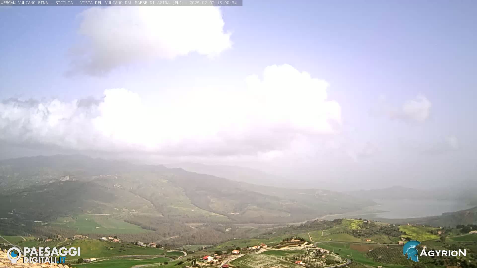A hazy, partly cloudy day reveals a panoramic view of rolling green hills and valleys, with a body of water visible in the distance.