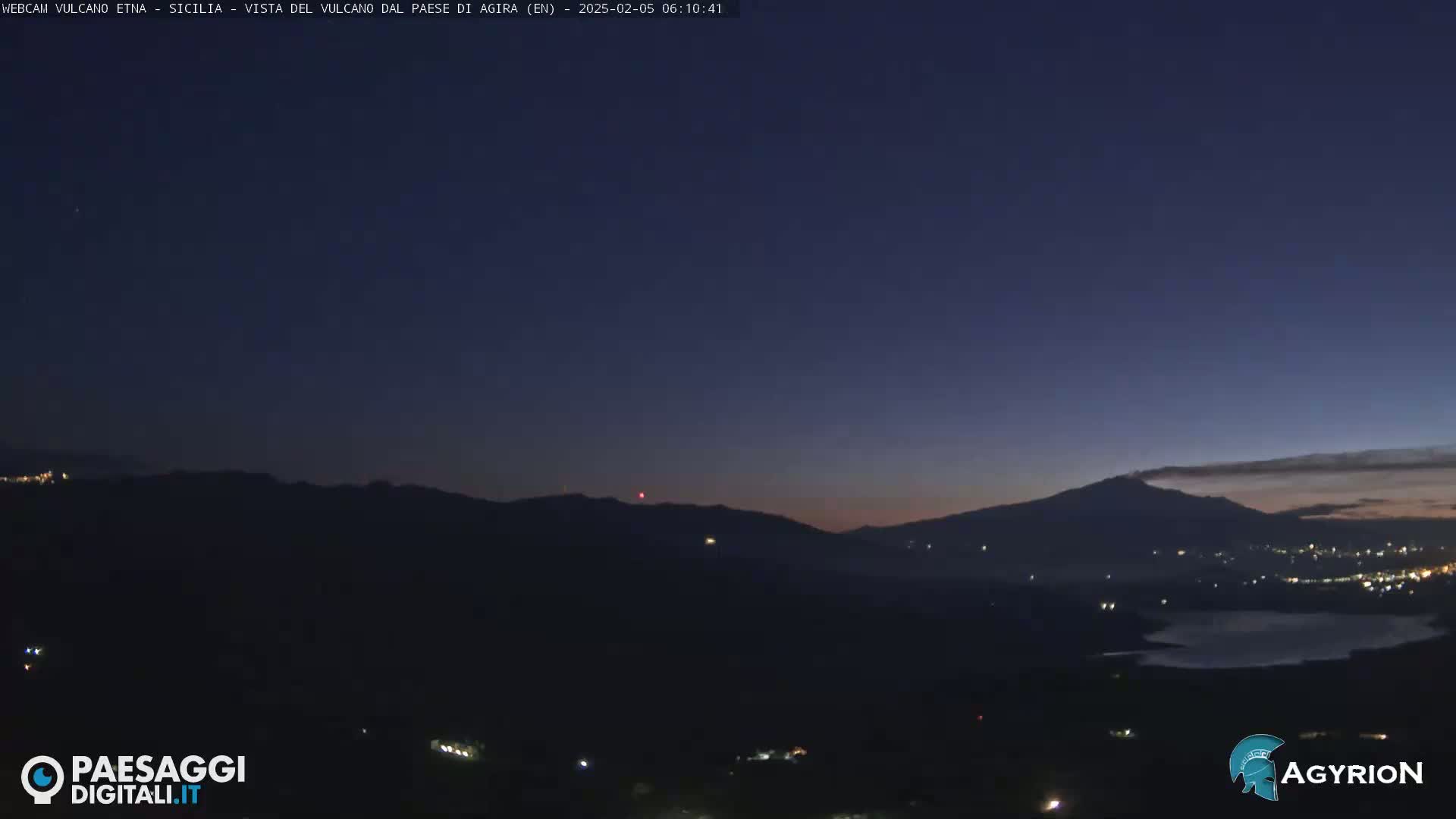 A dark, nighttime landscape shows a distant, silhouetted volcano under a twilight sky.