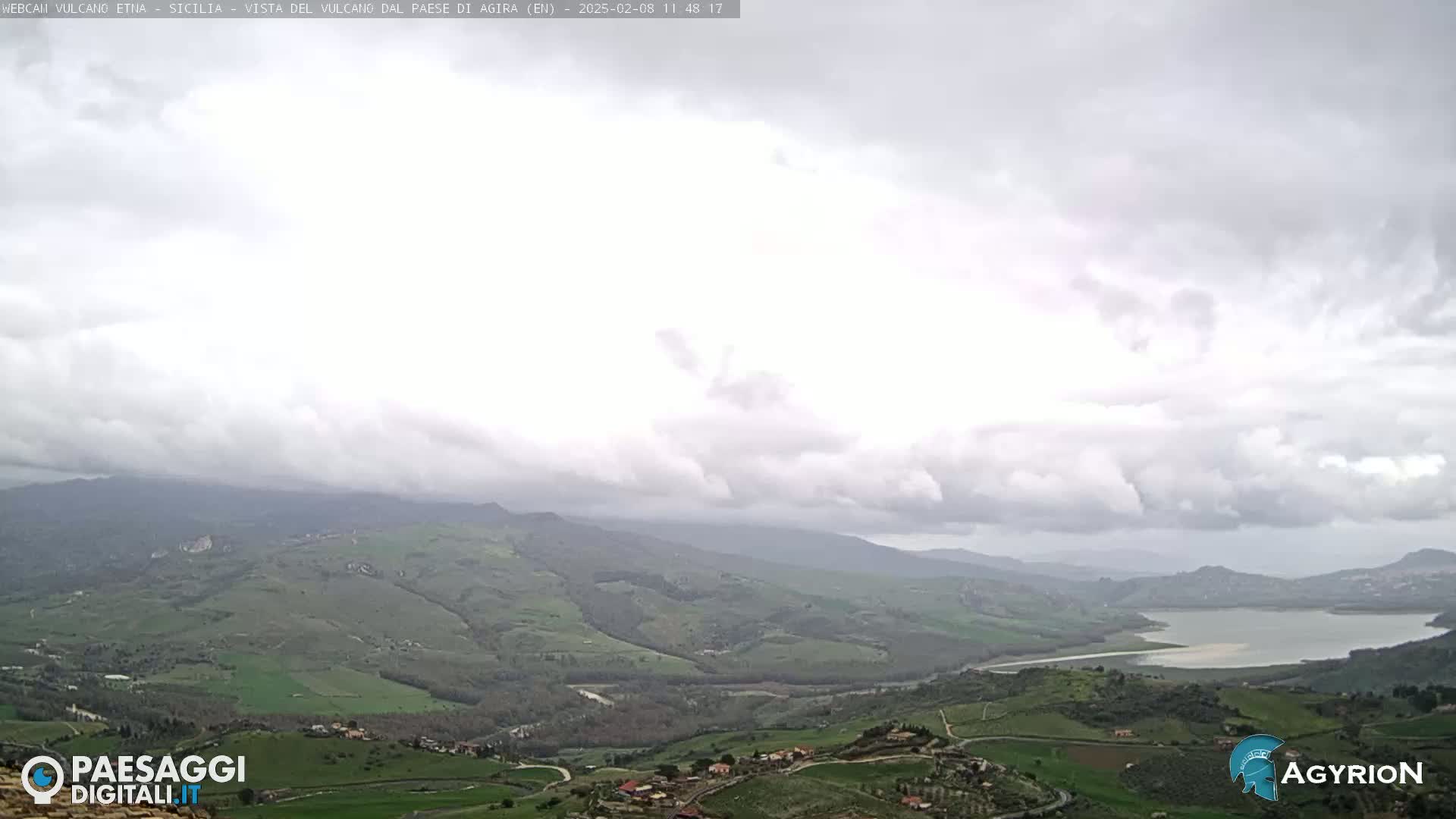 A view of a valley with rolling green hills and a body of water under an overcast sky.