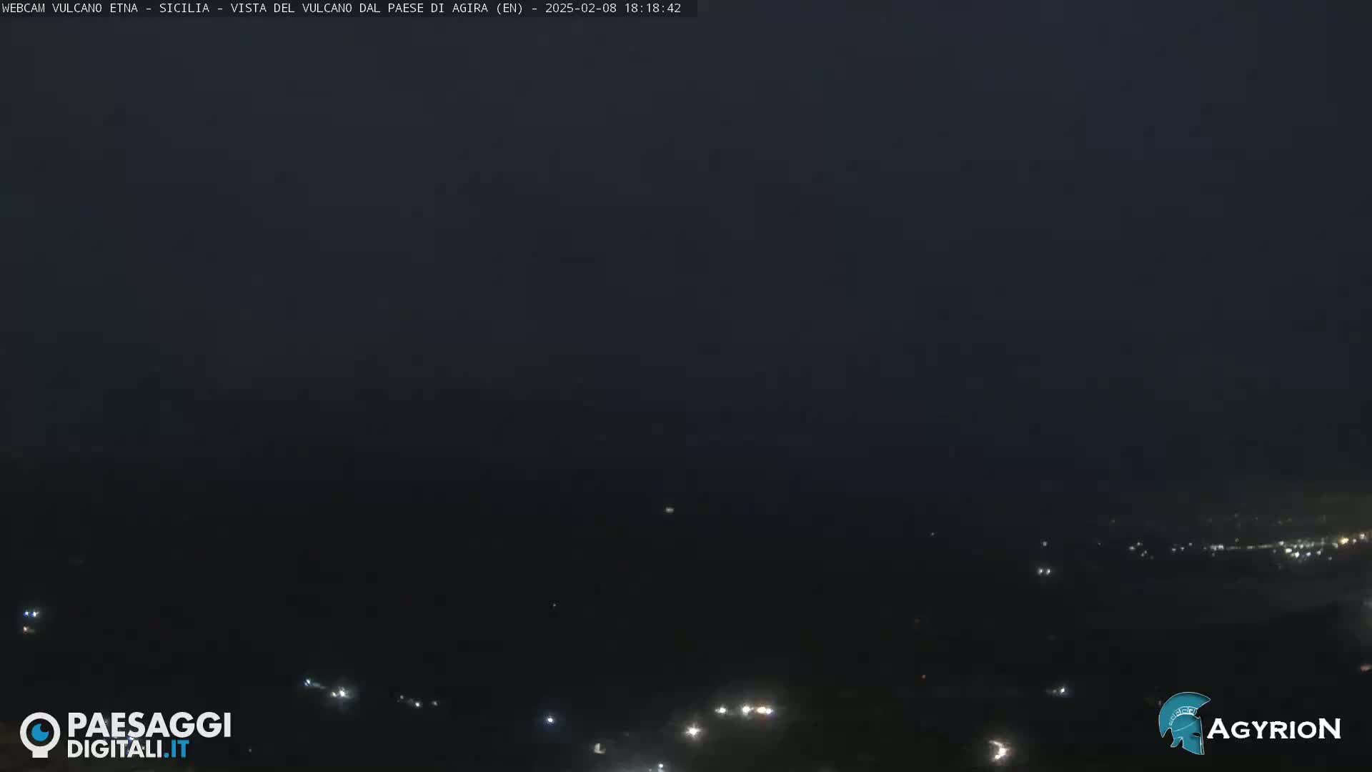 A nighttime, long shot of a dark landscape with a few small lights visible in the distance under a dark sky.