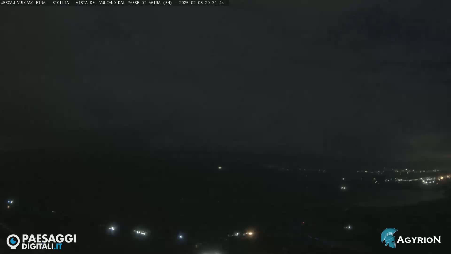A nighttime long shot of a dark, sparsely lit landscape, possibly a town or village, under a mostly clear, dark sky.