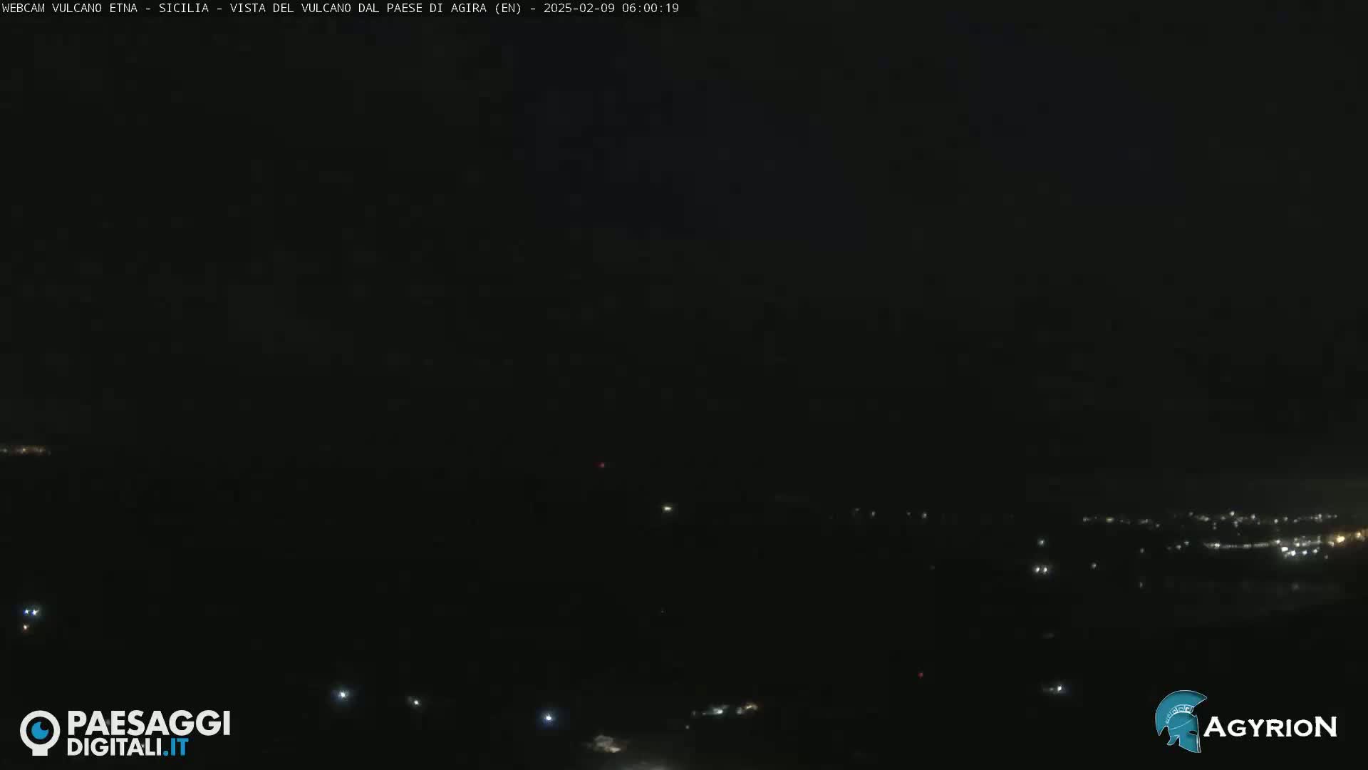 A nighttime long shot shows a dark landscape with sparsely scattered lights in the distance under a dark sky.