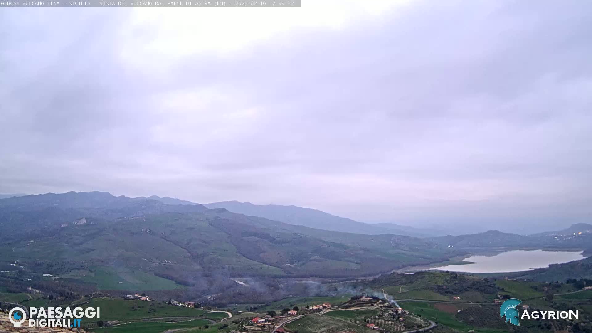 A panoramic view of rolling green hills and a lake under an overcast sky.